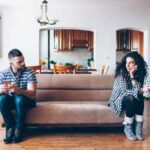 Couple in conflict sitting on sofa at home, using smart phones.