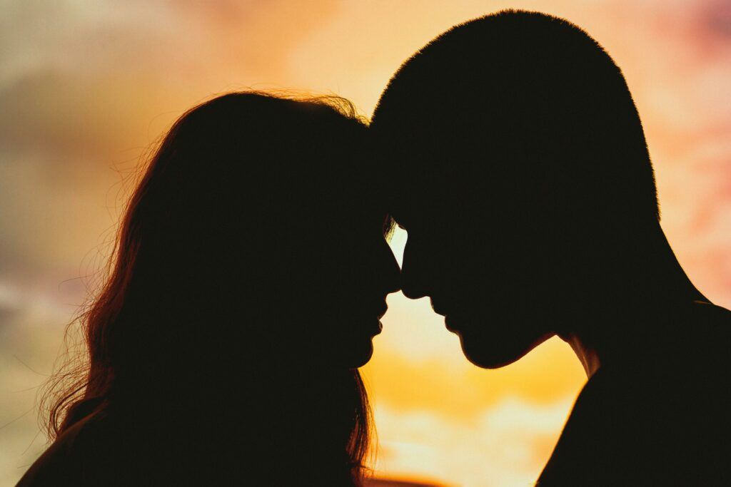 A couple with there foreheads together with a sunset in the background.