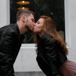 A couple shares a passionate kiss on a sidewalk outside a cafe.