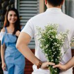 A man surprises his partner with flowers behind his back, symbolizing love and romance.