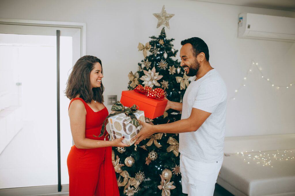 A couple exchanging gifts in front of a Christmas tree.