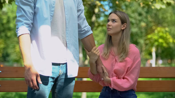 Man leaving upset girlfriend alone on bench in park walking away, break-up