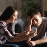 Girlfriend asking for explanation of her boyfriend sitting on a couch in the living room in a house interior with a dark background