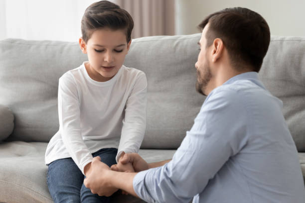 Worried loving young single father holding hand talking comforting upset little kid son sharing helping with problem of divorce.