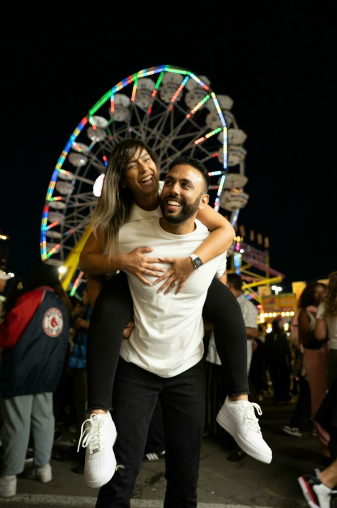 A couple at the fair with the Ferris Wheel in the background. and he's giving her a piggy back. Fun Date Ideas for Couples