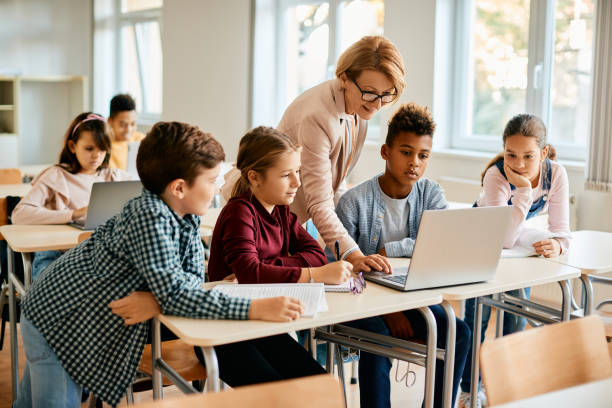 Elementary teacher and her students using laptop during computer class at school.