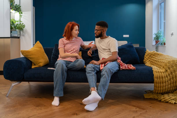 Emotional multi ethnic annoyed stressed couple sitting on couch effectively communication at home. Man and woman talking face to face trying come to agreement. Misunderstanding, relationship crisis, problems concept.