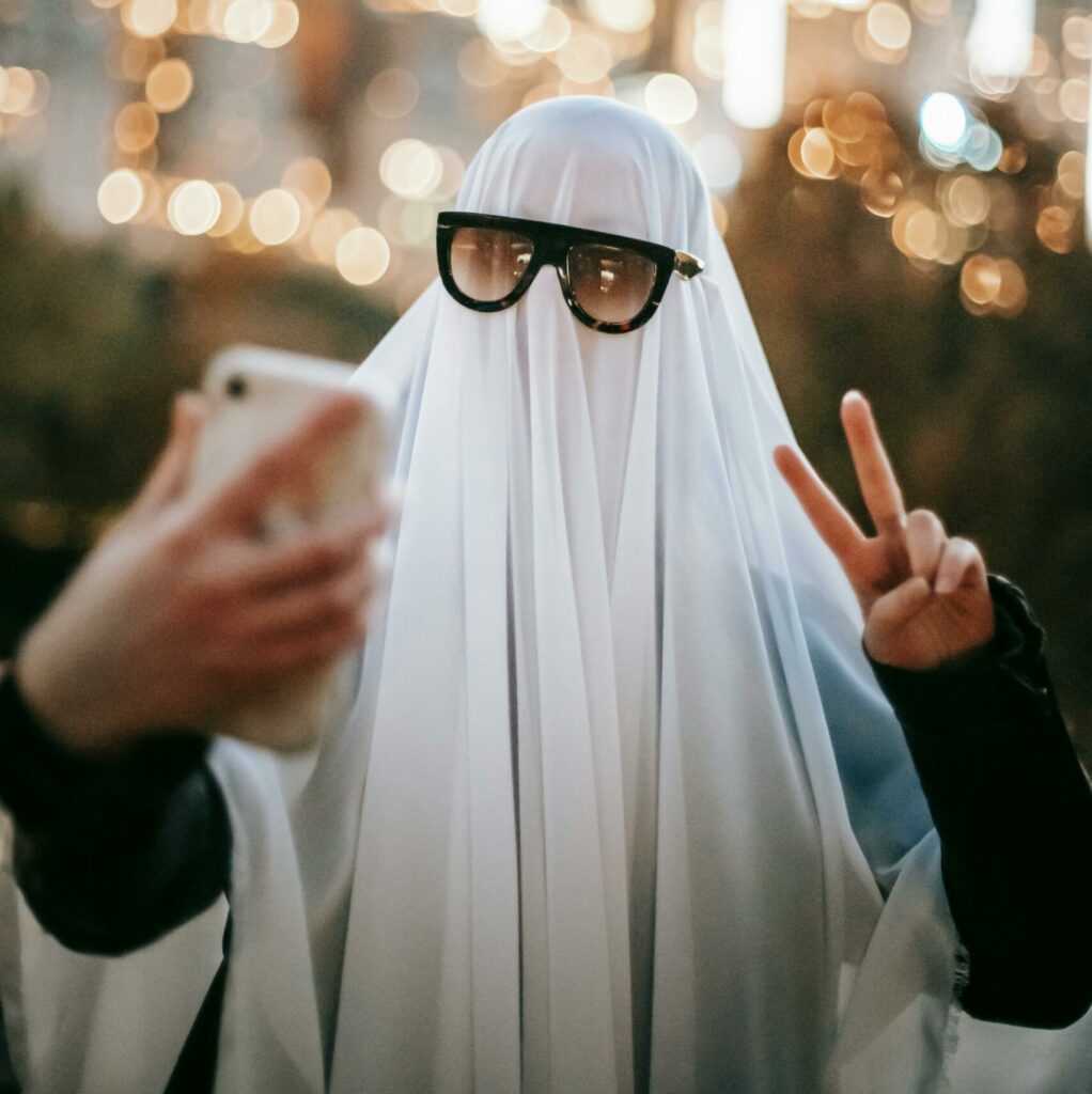 A person with a sheet over their head with sunglasses giving the peace sign into a phone. Why do People Ghost in Dating?