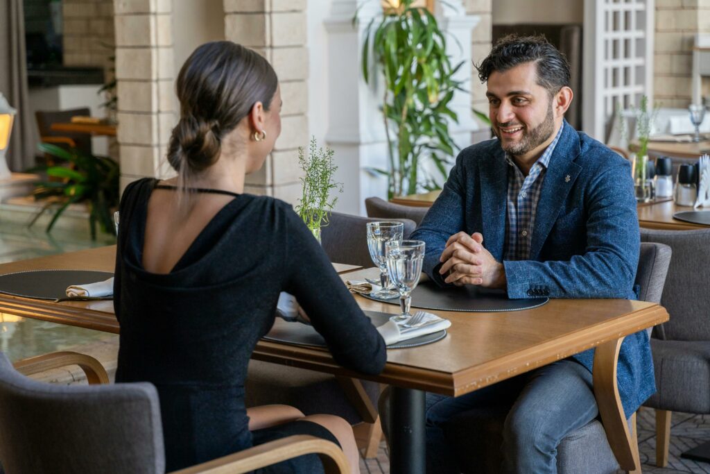 A woman and a man facing each other talking at a restaurant on their first date.