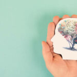 Hands holding paper head, human brain with flowers, self care and mental health concept, positive thinking, creative mind