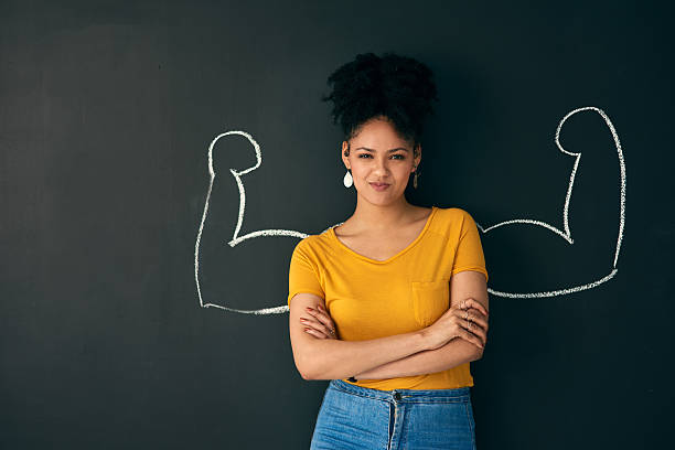 Shot of a woman posing with a chalk illustration of flexing muscles against a dark background. How to Build Self Confidence and Self Esteem