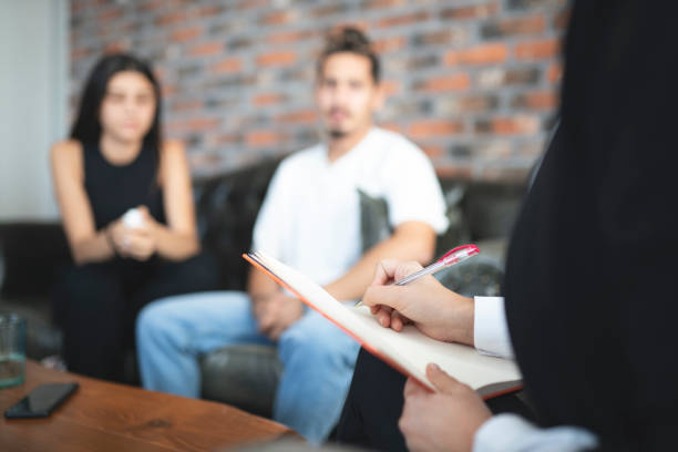 Young couple having session with psychologist at office. Psychologist is talking about problems. Young couple is listening to her.