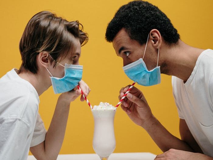 Couple sharing a milkshake while wearing masks, symbolizing love during pandemic.