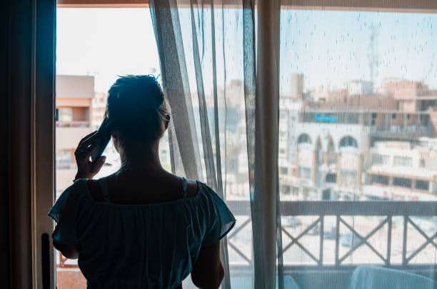 Woman rear view at home by the window in self isolation due to a separation from boyfrien. She talking on the phone.