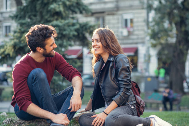 Happy couple talking while sitting on a meadow on their first date.