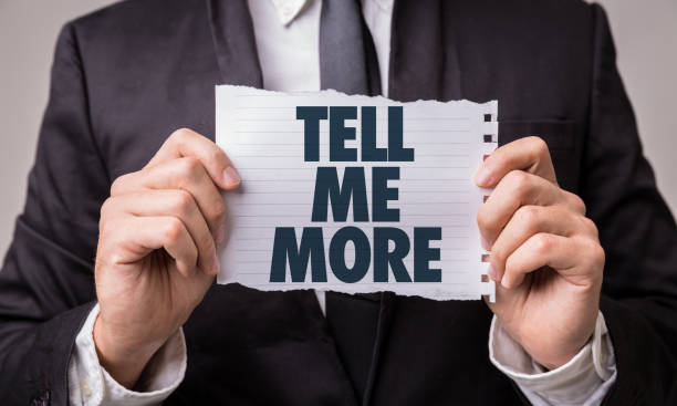 A man holding a piece of paper that says "Tell me more"